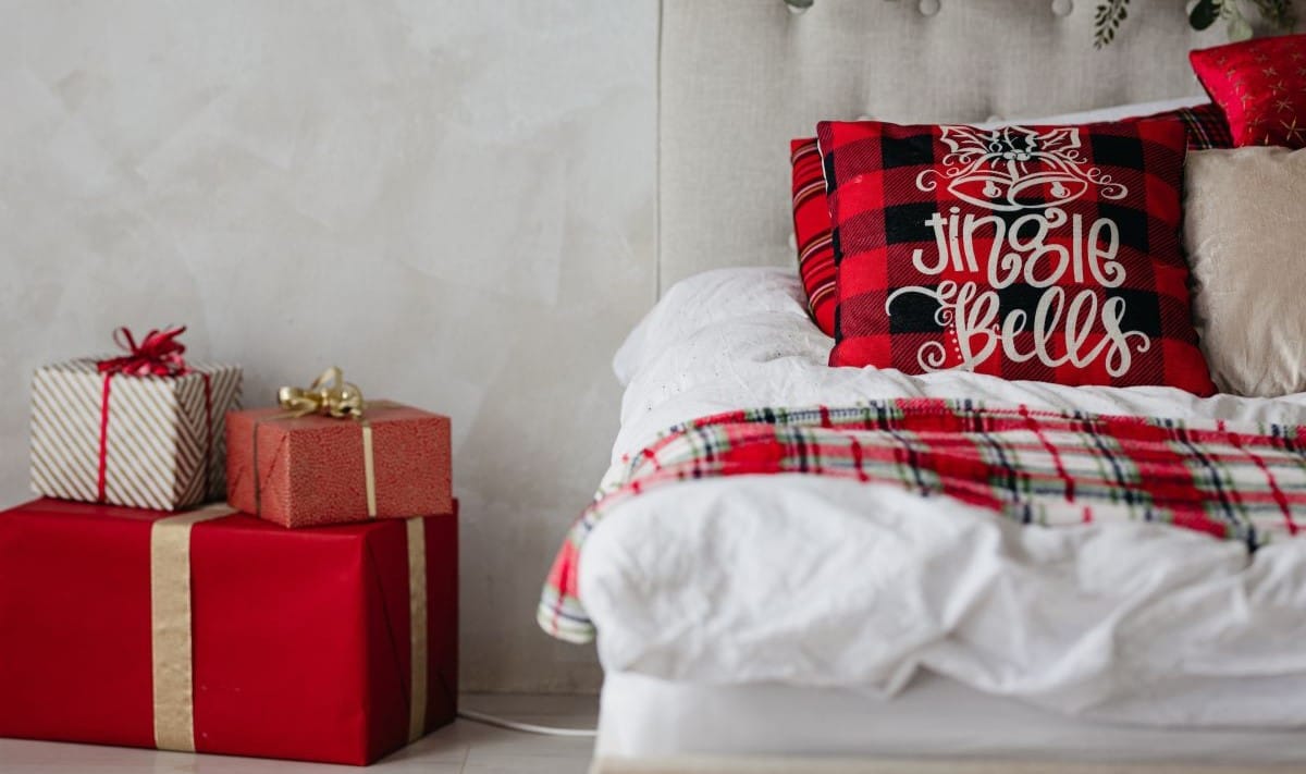 a bed decorated with red festive cushions and boxes wrapped in red paper with ribbons next to it